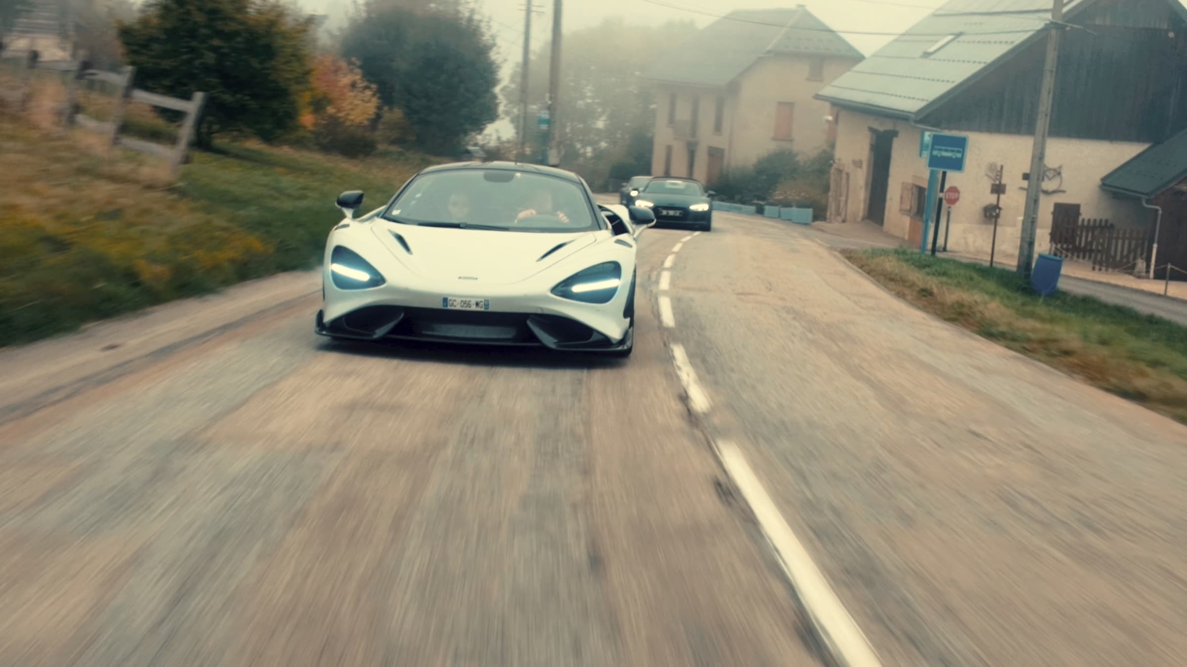 McLaren 765LT blanche en pleine accélération sur une route de village